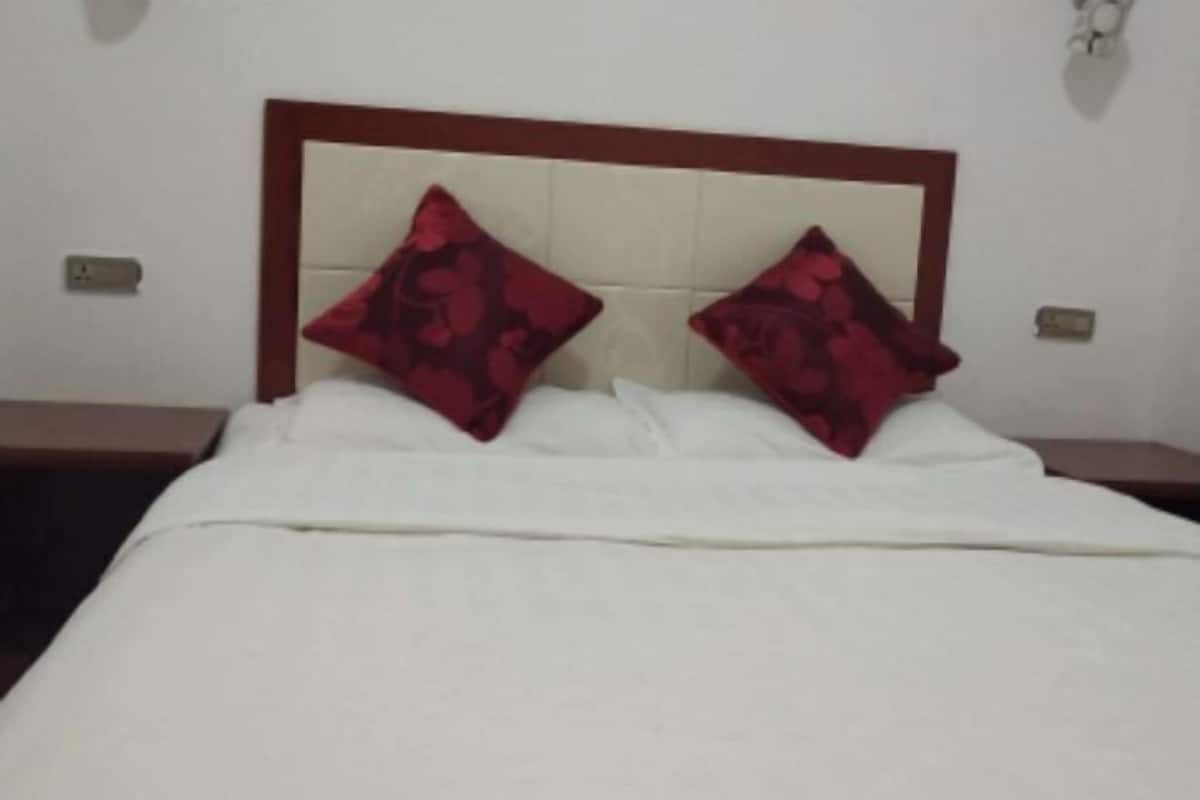 Una cama con cabecera de madera, ropa de cama blanca y dos almohadas rojas.