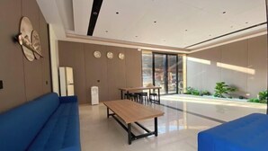 Un moderno vestíbulo de hotel con un sofá azul, una mesa de madera y un ventanal que ofrece vistas al follaje exterior.