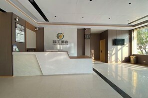 A reception area with a reception desk, a wall-mounted television, and a window providing natural light. - Liwang Hotel (Libo)