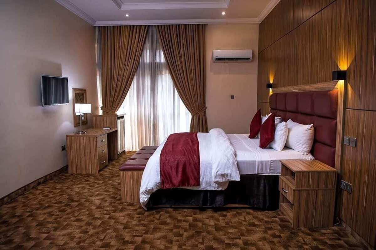 Une chambre d’hôtel avec un grand lit, un bureau en bois, un téléviseur à écran plat et une fenêtre avec des rideaux.