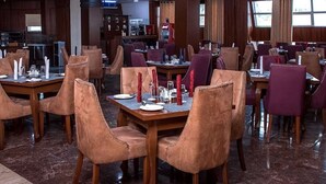 A restaurant with wooden tables and chairs, marble flooring, and a kitchen area in the background. - Elegant Hotel by Best Western Plus  (Enugu)