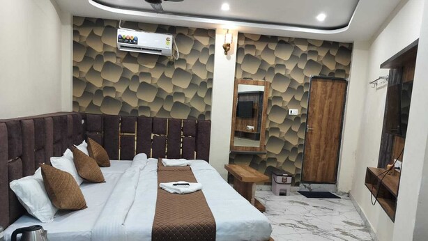 A modern bedroom with a large bed, a wooden headboard, a marble floor, a built-in TV, and a wardrobe. - Hotel Mahalok Palace (Ujjain)