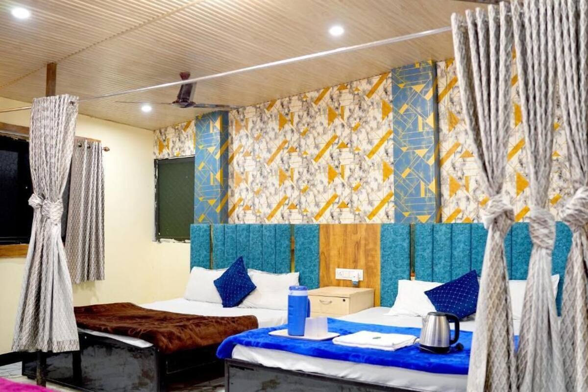 Ein Hotelzimmer mit Bett, Nachttisch, blauer Decke, Wasserkocher und Vorhängen.