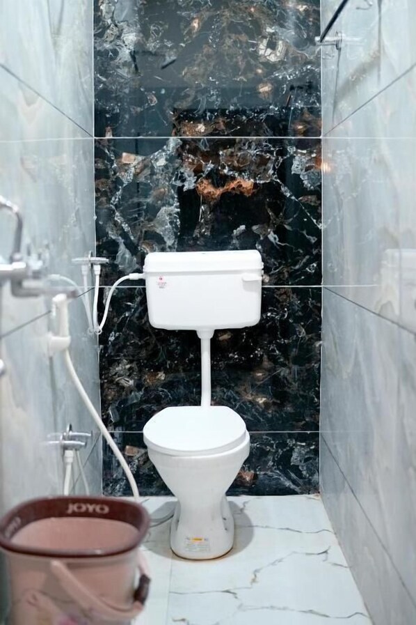 A bathroom with a white toilet, marble walls, and a marble floor. - Hotel Mahalok Palace (Ujjain)