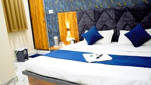 A hotel room with a large bed, a wooden headboard, a nightstand with a lamp, and a patterned wall. - Hotel Mahalok Palace (Ujjain)