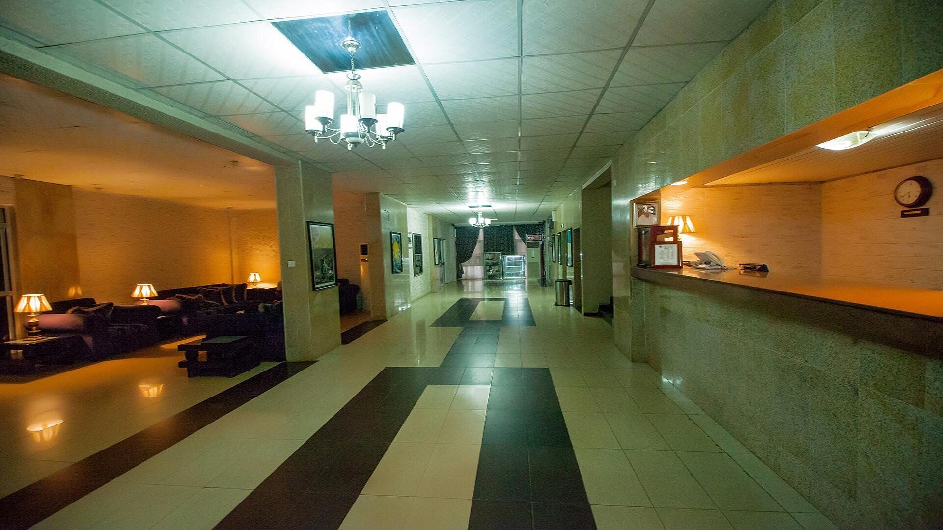 A hotel lobby with a reception desk, a seating area with couches, and a chandelier.