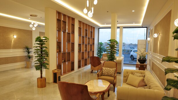 A spacious lobby with a high ceiling, a central seating area with a sofa and chairs, a large wooden bookshelf, and potted plants. - alzuwain hotil (Arar)