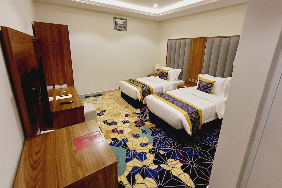 Ein Hotelzimmer mit zwei Betten, einem Holztisch und einem gemusterten Boden.