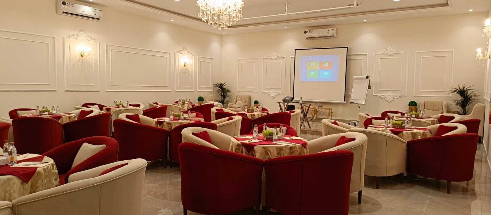 Une salle de conférence équipée de plusieurs tables et chaises, d’un écran de projection et d’appliques murales décoratives.