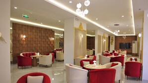 A modern hotel lobby with red and white armchairs, a wooden wall, and a television screen. - alzuwain hotil (Arar)