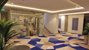 A modern hotel lobby with a geometric patterned carpet, marble walls, and a staircase. - alzuwain hotil (Arar)
