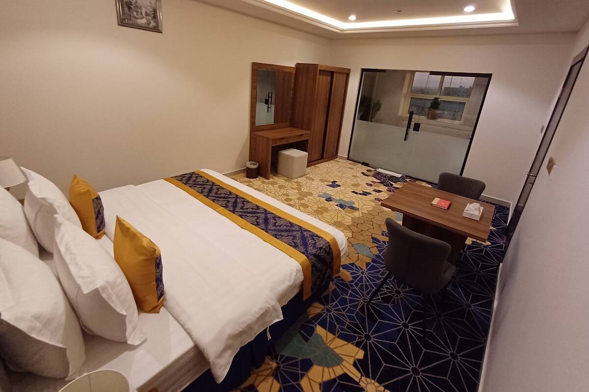 Ein Hotelzimmer mit Bett, Schreibtisch, Stuhl, Spiegel und Fenster.