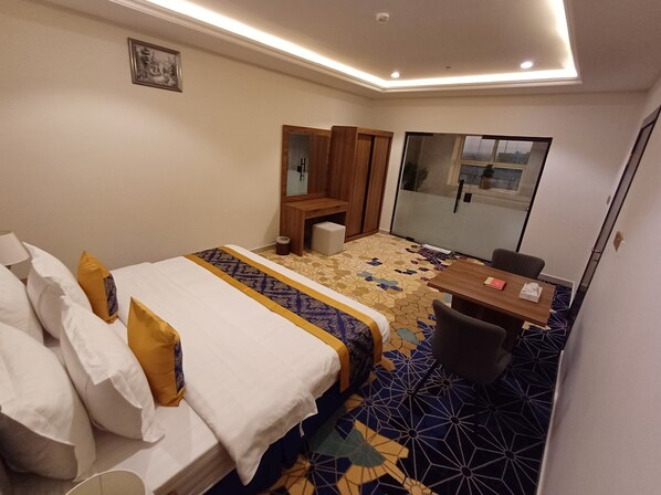 Une chambre d’hôtel avec un lit, un bureau, une chaise, un miroir et une fenêtre.