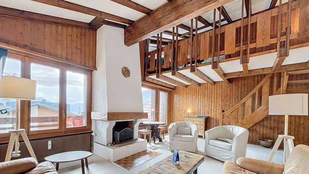 Ein gemütliches Wohnzimmer mit Kamin, Holzbalken und großen Fenstern.