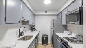 Une cuisine de taille réduite avec des meubles blancs, un évier en acier inoxydable, une cuisinière et un four à micro-ondes.