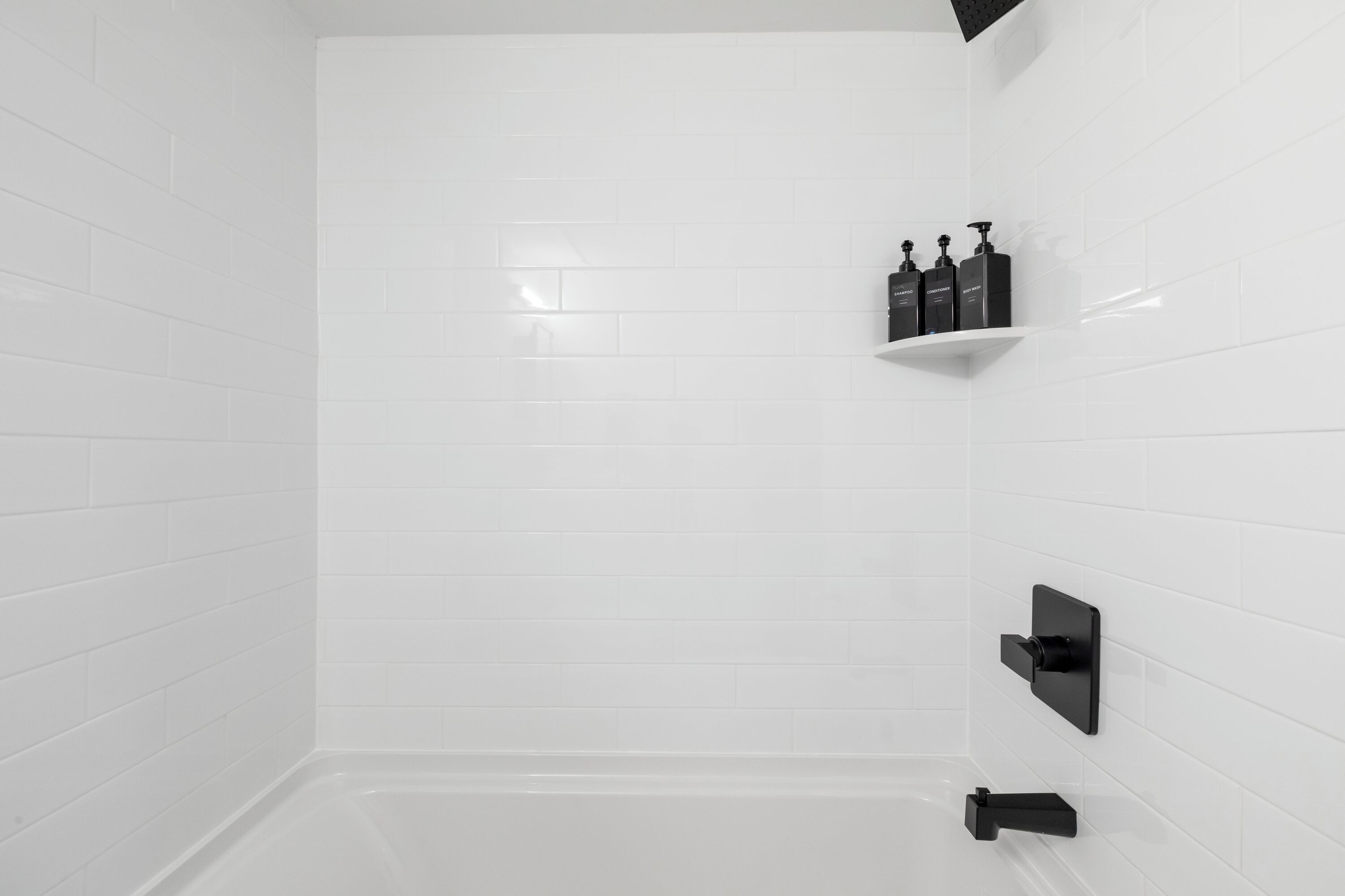 Ein modernes Badezimmer mit weißen Fliesen, einem schwarzen Ablagefach mit Pflegeprodukten und einem schwarzen Wasserhahn.