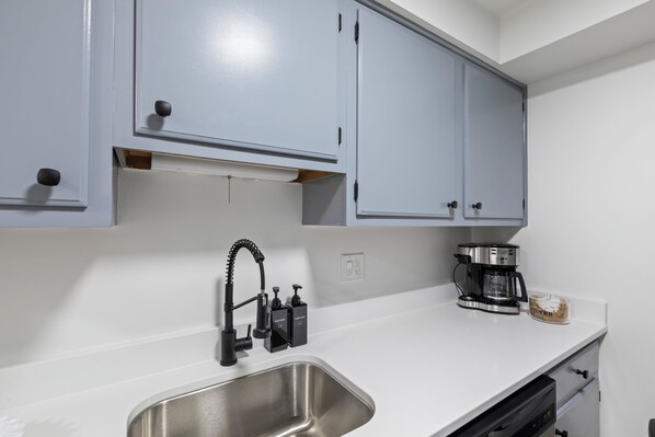 A kitchen with a stainless steel sink, a coffee maker, and a cabinet with a handle.