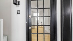 Une porte noire ornée d’un motif quadrillé, une plaque portant le numéro « 101 », et un luminaire placé au-dessus.
