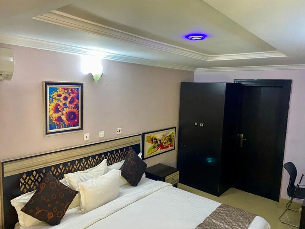 A hotel room with a bed, nightstands, a wardrobe, and artwork on the walls.