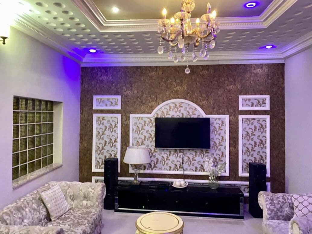 Una sala de estar con sofá, televisor montado en la pared, candelabro y un papel tapiz estampado.