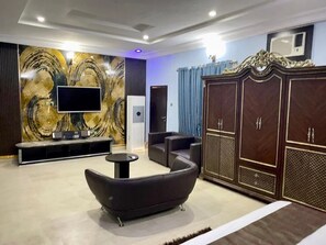 A modern living room with a flat-screen TV, a sofa, a cabinet, and a decorative wall. - Garden Atlantis Hotel (Enugu)
