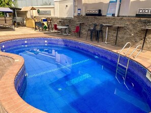 A swimming pool with a tiled edge, lounge chairs, and a small table. - Garden Atlantis Hotel (Enugu)