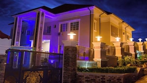A two-story house with a covered porch and a stone wall in front. - Garden Atlantis Hotel (Enugu)