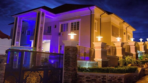 A two-story house with a covered porch and a stone wall in front. - Garden Atlantis Hotel (Enugu)