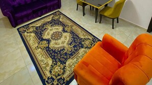A living room with a purple sofa, a yellow table, and an orange armchair. - Garden Atlantis Hotel (Enugu)