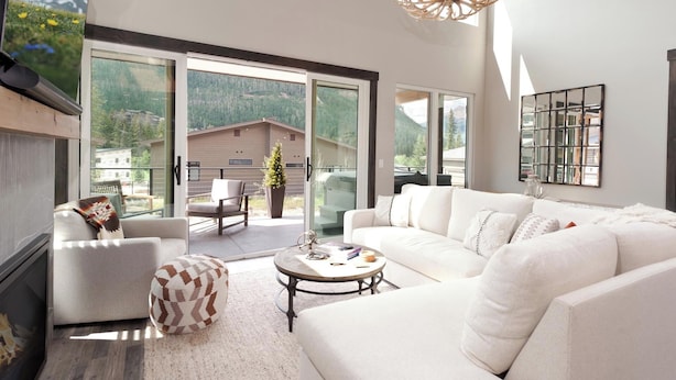 A spacious living room with a white sofa, a round coffee table, and a fireplace. Large windows offer a view of a mountainous landscape.