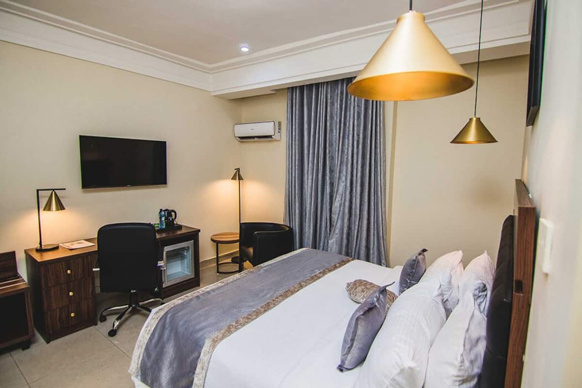 Ein Hotelzimmer mit Bett, Schreibtisch, Stuhl, Fernseher und Klimaanlage.