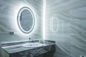Ein modernes Badezimmer mit Marmorwaschbecken, einem großen Spiegel mit runder Beleuchtung und einer Wand mit Marmoroptik.