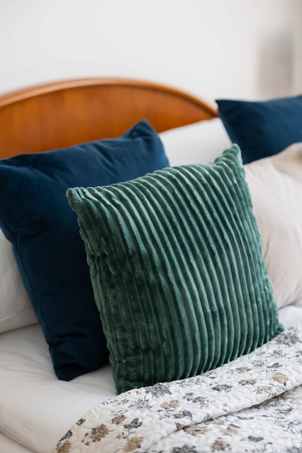 Un lit avec une tête de lit en bois, un oreiller vert à texture et une couverture à motifs floraux.