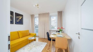 A compact living space with a yellow sofa, a dining table with chairs, and a view of the city through large windows.