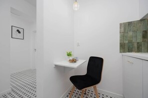 Une salle de bain moderne avec une chaise noire, une petite étagère blanche ornée d’une plante et un mur recouvert de carreaux.