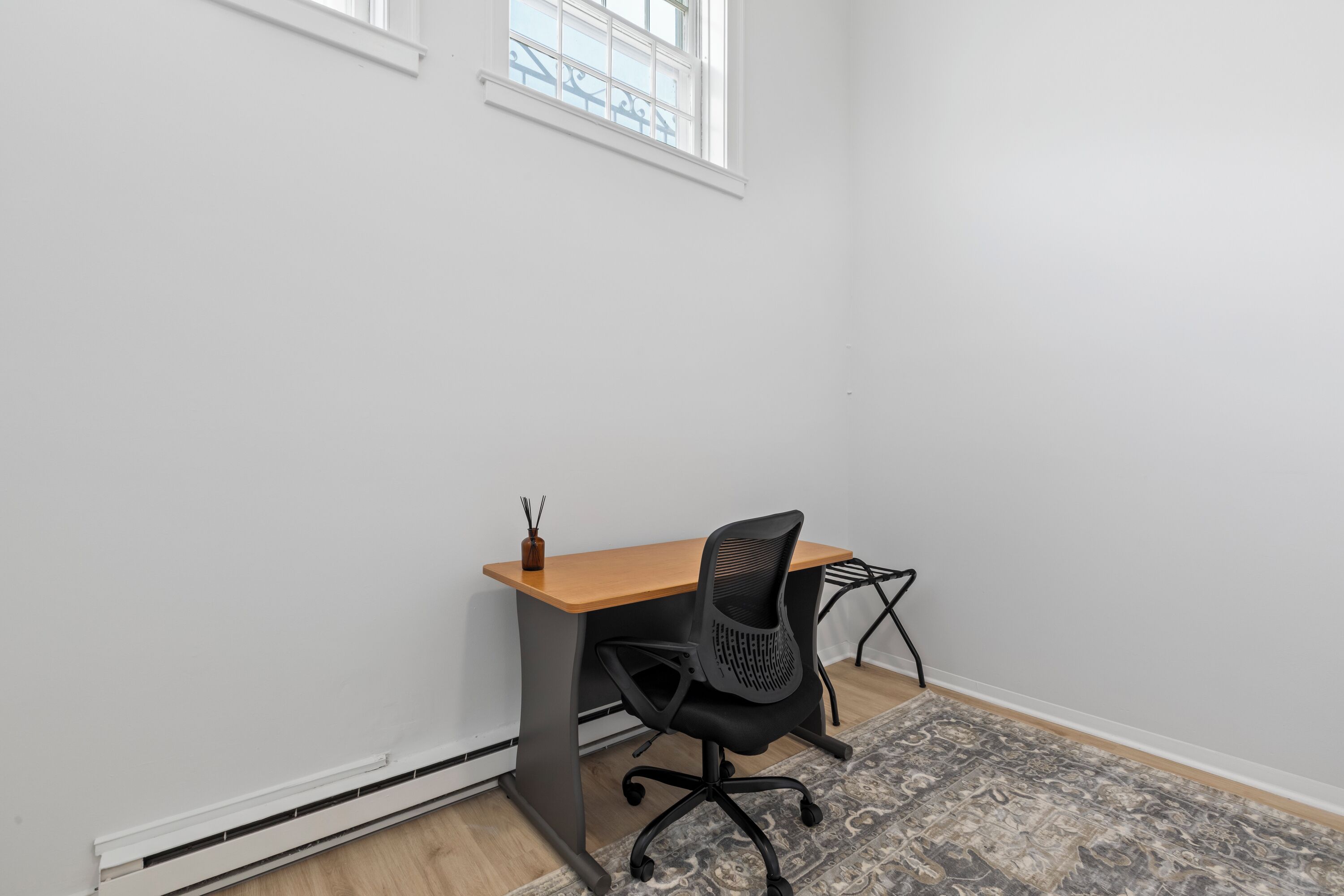 Une petite pièce propre, avec un bureau en bois, un fauteuil de bureau noir et un tapis à motifs.