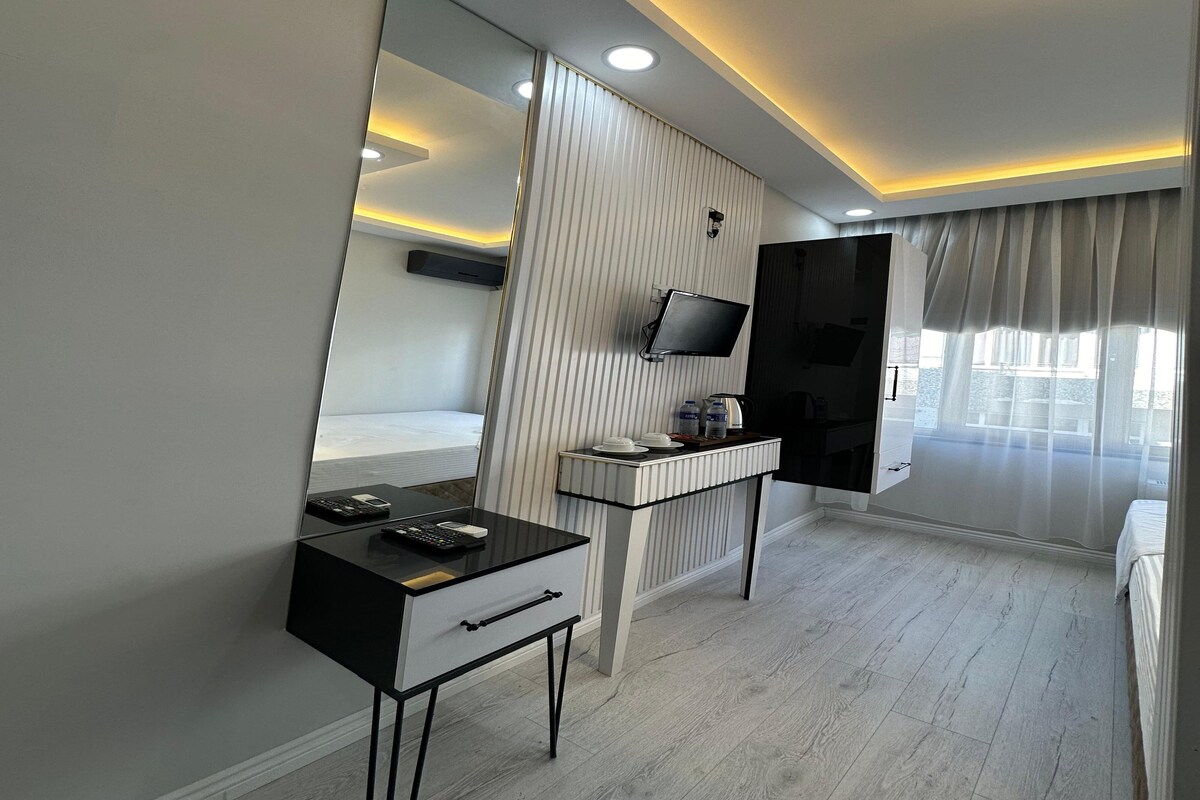 Een moderne hotelkamer met een grote spiegel, een bureau met een flatscreen televisie, een bed en een raam met gordijnen.