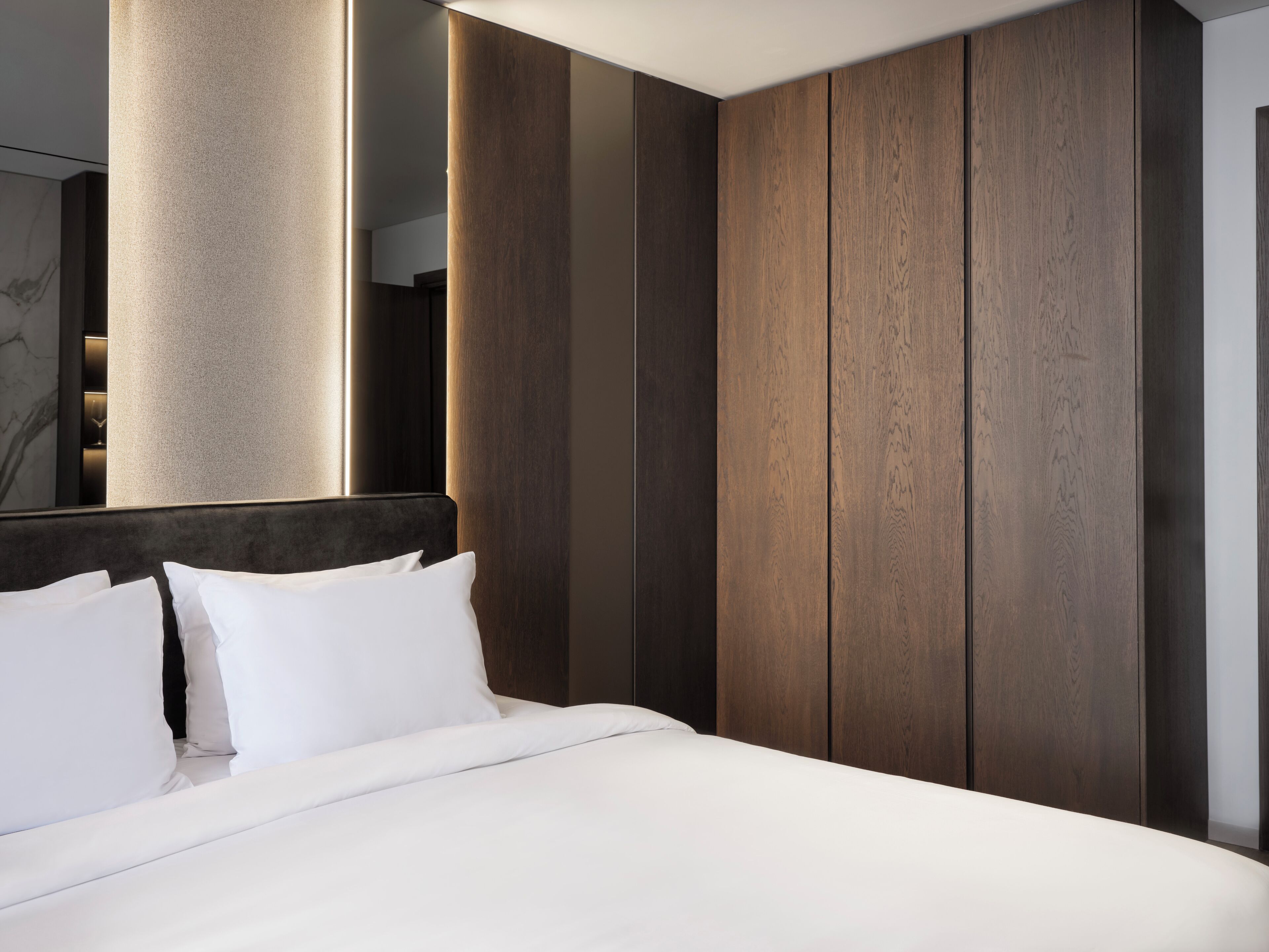 Una habitación de hotel moderna con una cama grande, paneles de madera oscura y una columna imponente.