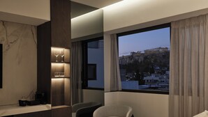Een moderne hotelkamer met een bed, een bureau, een stoel en een groot raam met uitzicht op een historisch pand.