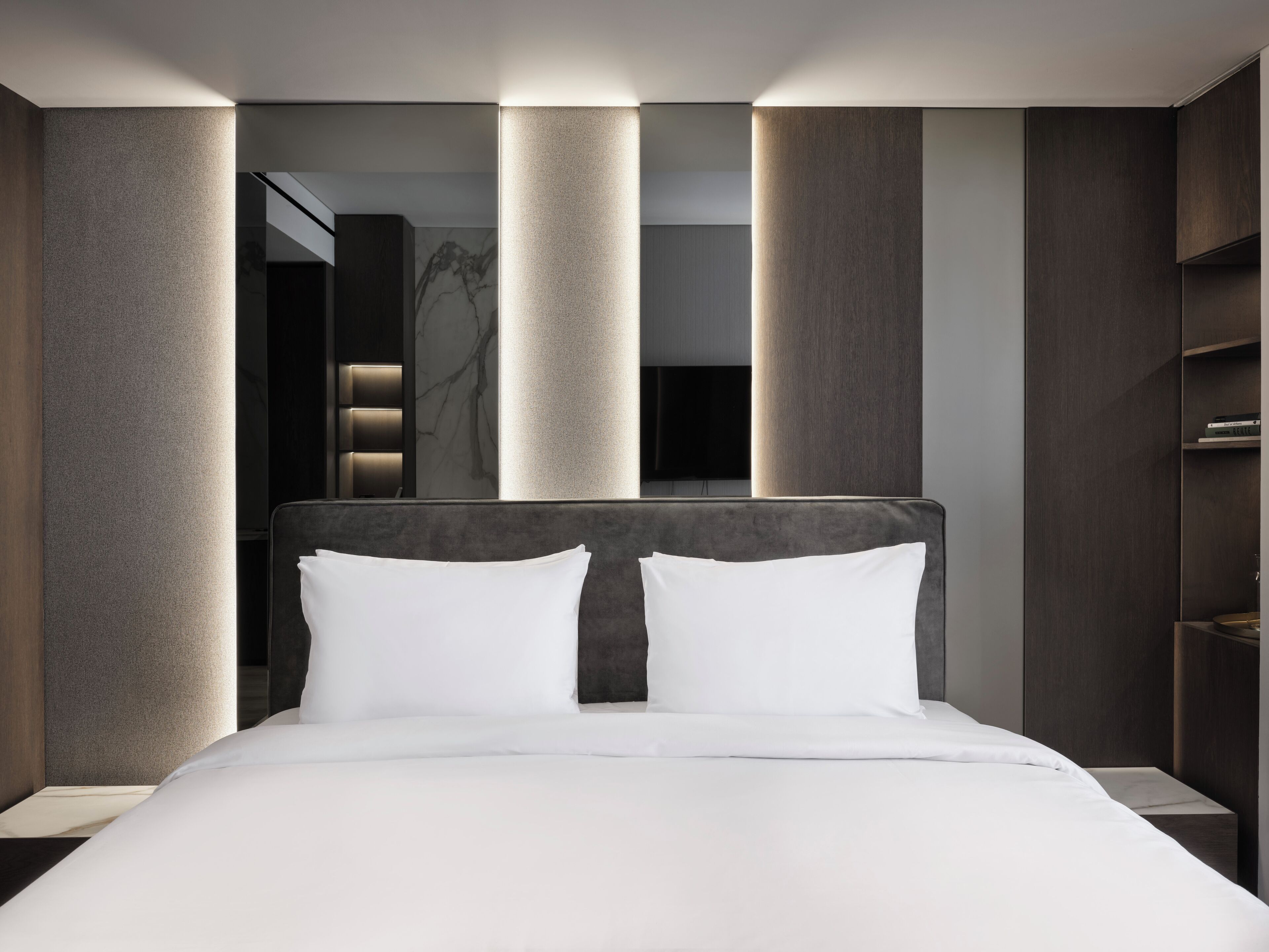 A modern hotel room with a large bed, dark wood paneling, and a large mirror.