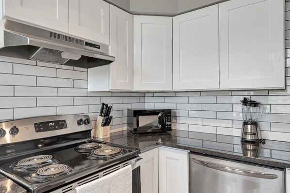 A modern kitchen with white cabinets, a stainless steel stove, a microwave, and a blender.