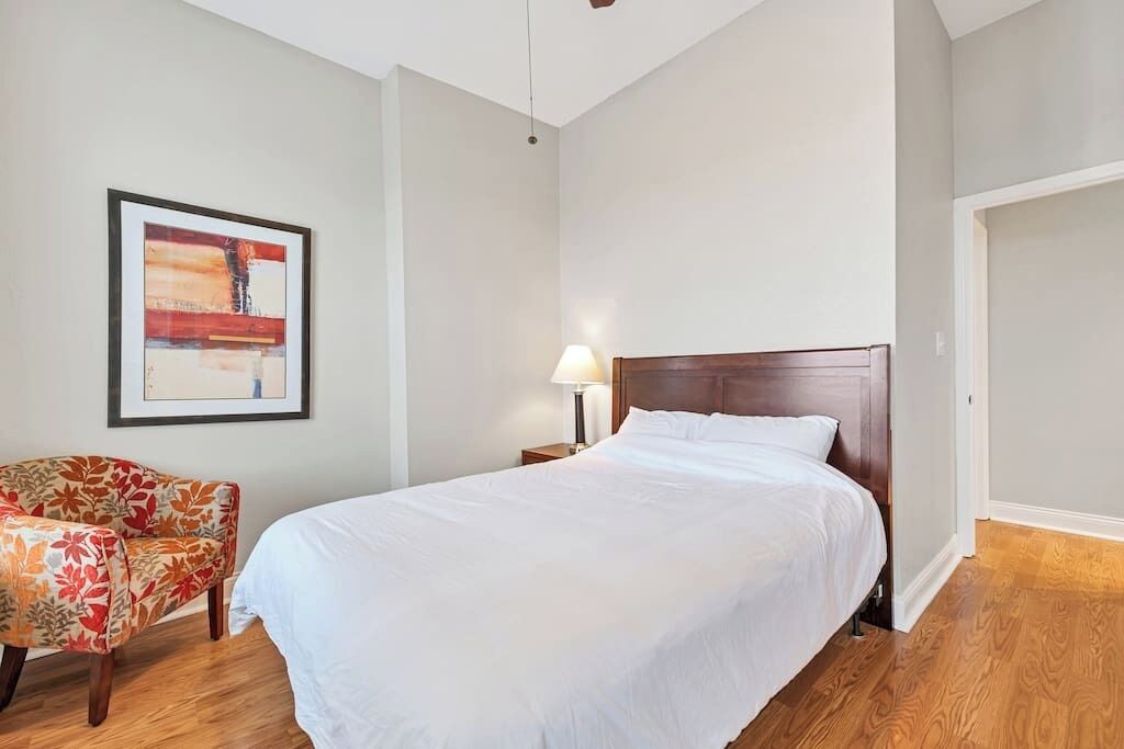A hotel room with a large bed, a chair, a nightstand, and a framed picture on the wall.