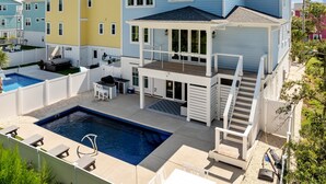 A multi-story house with a backyard pool, a covered patio, and a staircase leading to the upper floor. - Seas the Day, gorgeous private home, heated pool (Kure Beach)