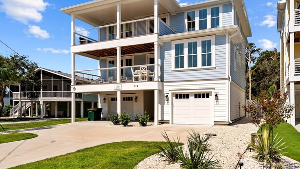 A two-story house with a covered front porch, a garage, and a well-maintained lawn. - Seas the Day, gorgeous private home, heated pool (Kure Beach)