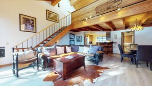 A spacious living room with a leather sofa, a wooden coffee table, and a cowhide rug. A staircase with wooden railings leads to an upper level. - Large Townhouse, Washer/Dryer, Quiet Location. Pool & Tennis Courts On-site (Mammoth Lakes)