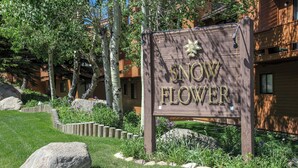 A wooden sign with the text "SNOW FLOWER" in gold lettering, surrounded by a landscaped garden with large rocks and trees. - Large Townhouse, Washer/Dryer, Quiet Location. Pool & Tennis Courts On-site (Mammoth Lakes)