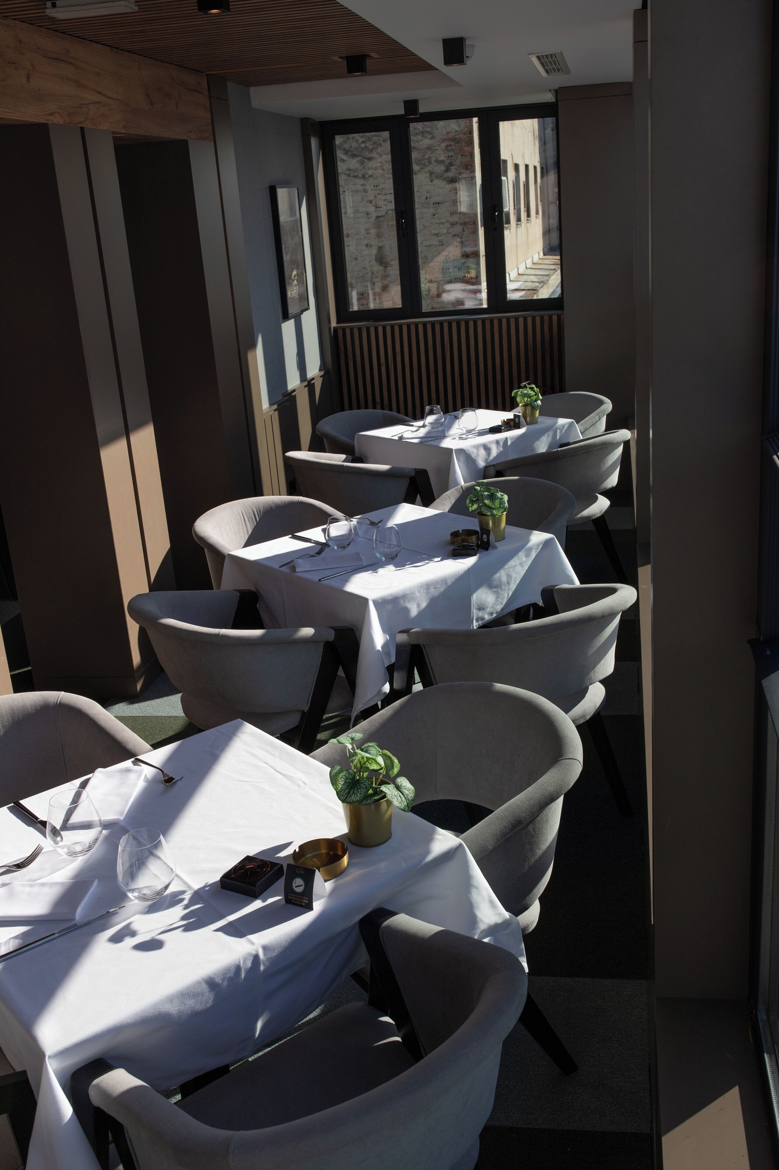 Ein Restaurant mit mehreren Tischen, gedeckt mit weißen Tischdecken, Stühlen und kleinen Topfpflanzen.