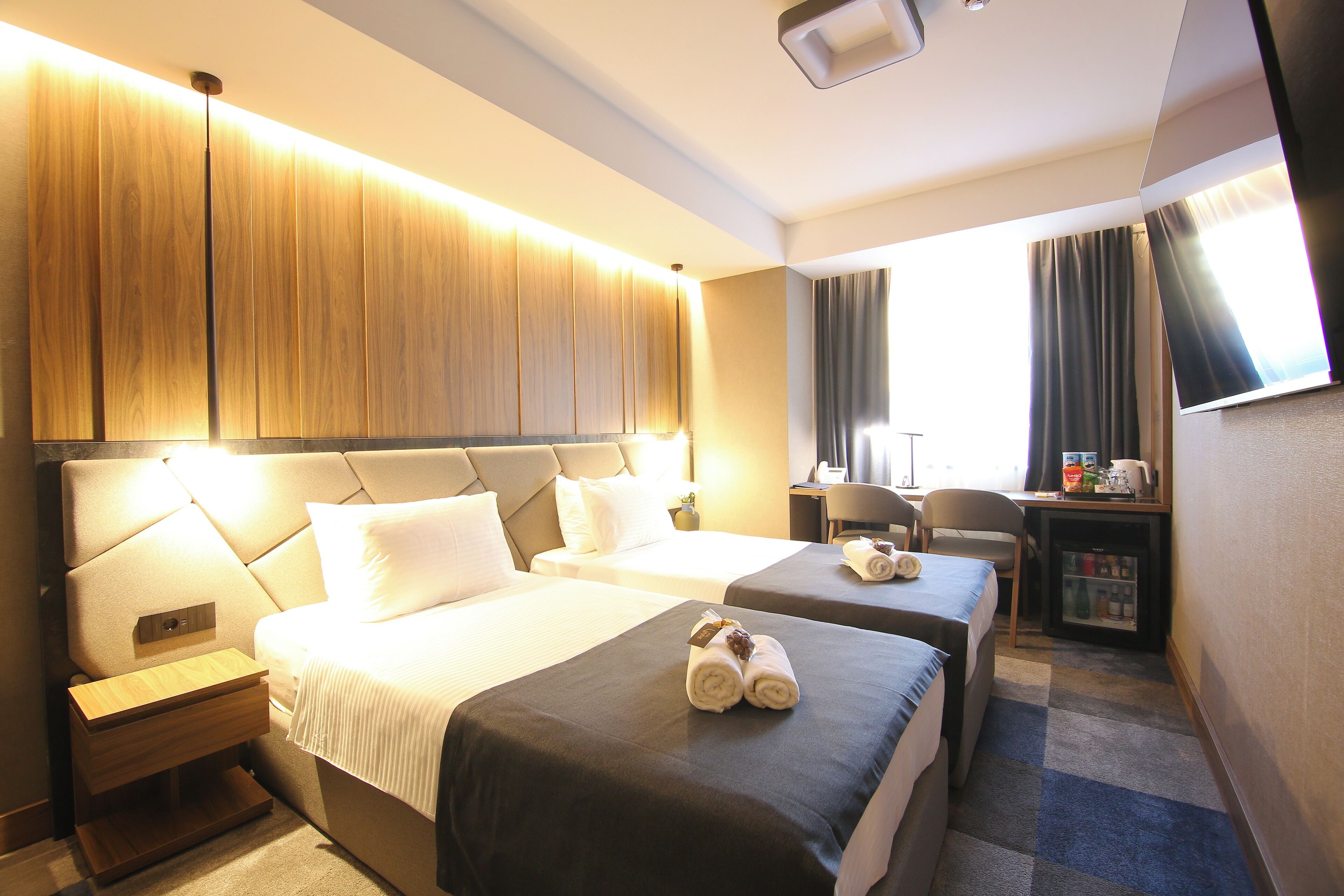 Habitación de hotel con dos camas, un escritorio, una silla y un televisor.