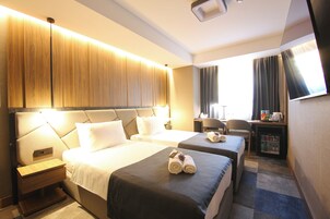 Habitación de hotel con dos camas, un escritorio, una silla y un televisor.