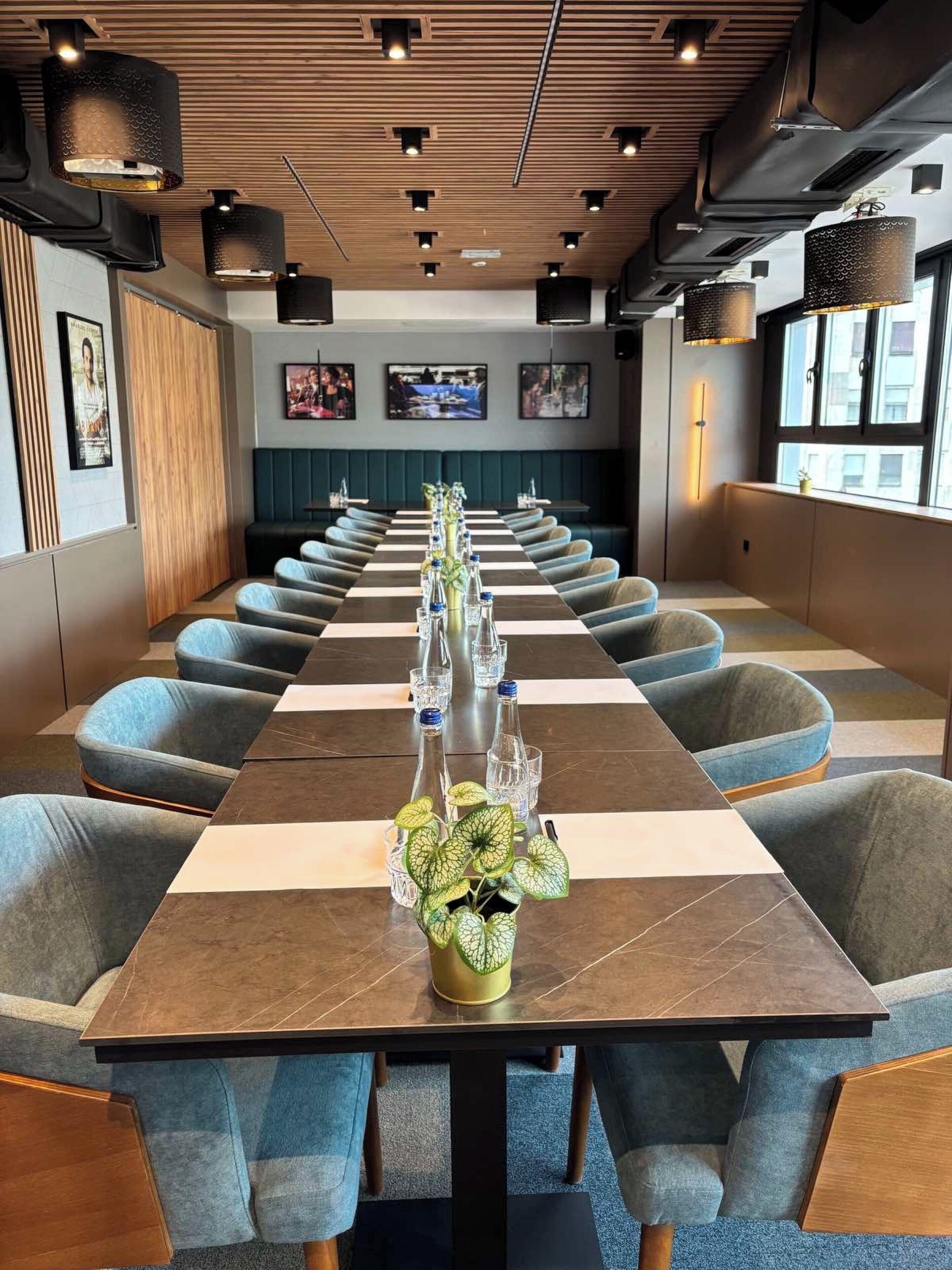 Un salón de conferencias con una larga mesa, sillas acolchadas en azul y un centro de mesa decorativo con planta.